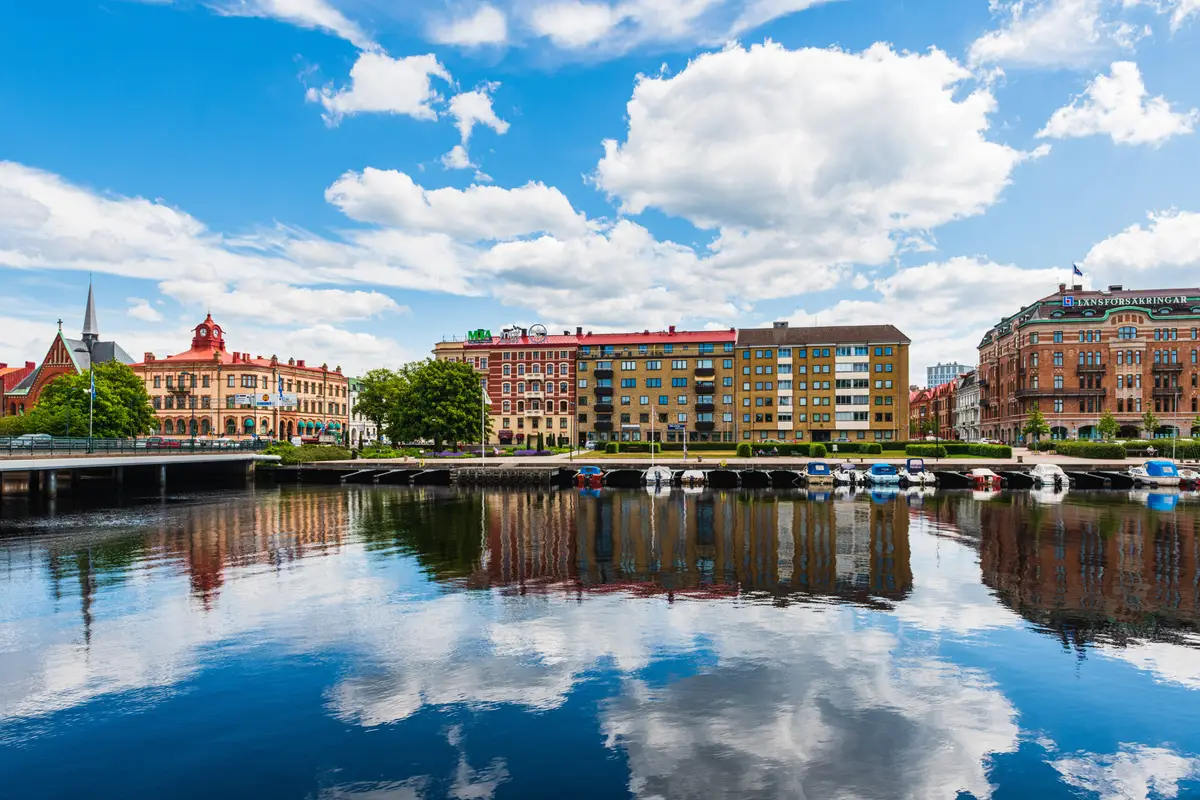 Colorful buildings lining the riverfront in Halmstad, Sweden, reflecting on the calm waters with a vibrant blue sky overhead.