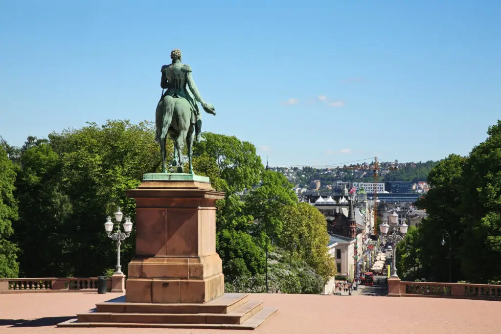 Bronze statue of King Charles John on horseback overlooking Karl Johans gate, Oslo, Norway, with clear blue sky and bustling city street in the background.