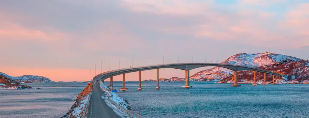 Sommaroy Bridge in Tromso, Norway, connecting Kvaloya and Sommaroy islands with scenic snowy landscapes and a glowing sunset.