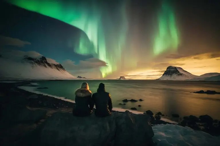 Tourists sitting on a rock observing the stunning Northern Lights in a snowy Norwegian landscape at night.