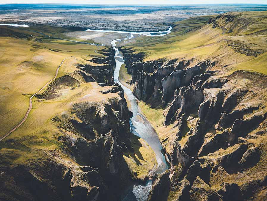 Aerial view of the stunning Fjaðrárgljúfur Canyon in Iceland, showcasing its deep green gorges and meandering river, perfect for nature enthusiasts and tourists exploring Scandinavian landscapes.