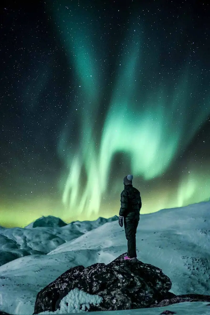Tourist standing under the mesmerizing Northern Lights in Iceland during a private night tour.
