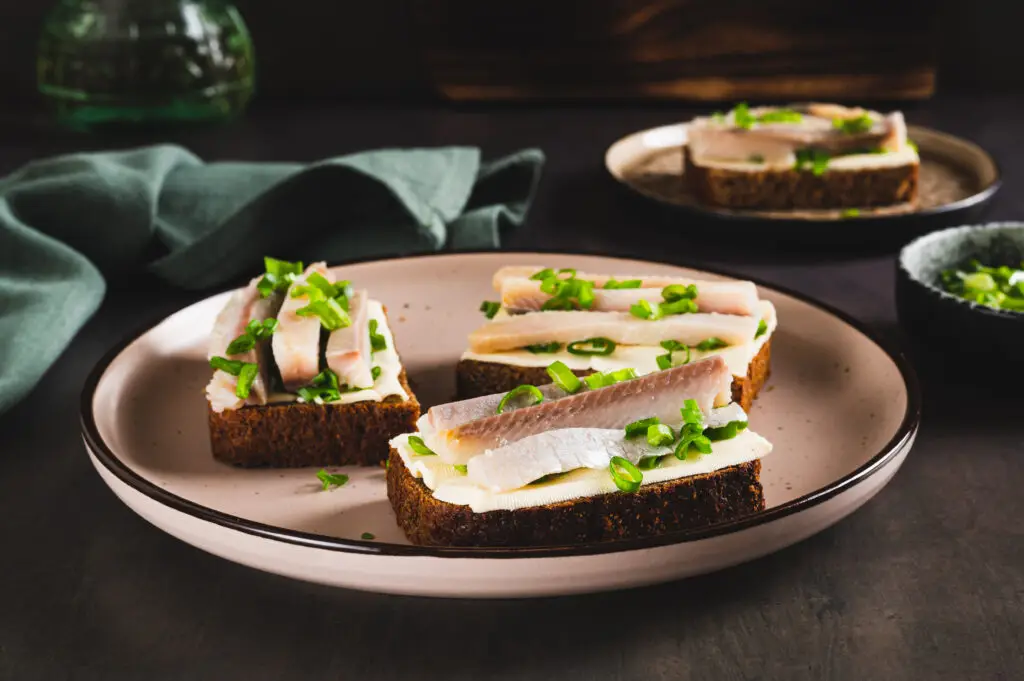 Traditional Scandinavian open sandwiches with salted herring, butter, and chives on rye bread, served on a ceramic plate, evoking the culinary heritage of Norway.
