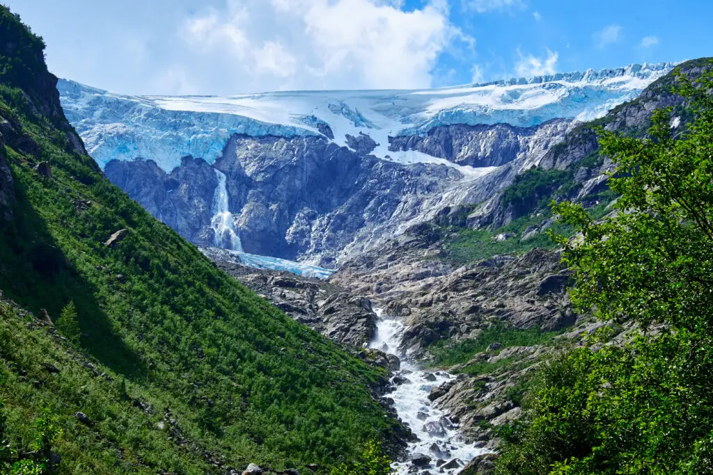 Breathtaking view up the canyon towards the blue ice of Folgefonna Glacier surrounded by rugged cliffs and greenery in Hardanger, Norway, showcasing natural Scandinavian beauty.