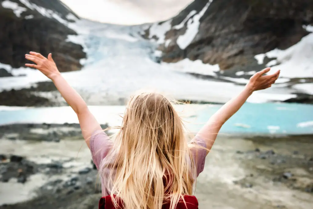 Solo female traveler with raised hands celebrating the view of Steindalsbreen Glacier in the Lyngen Alps, Norway.