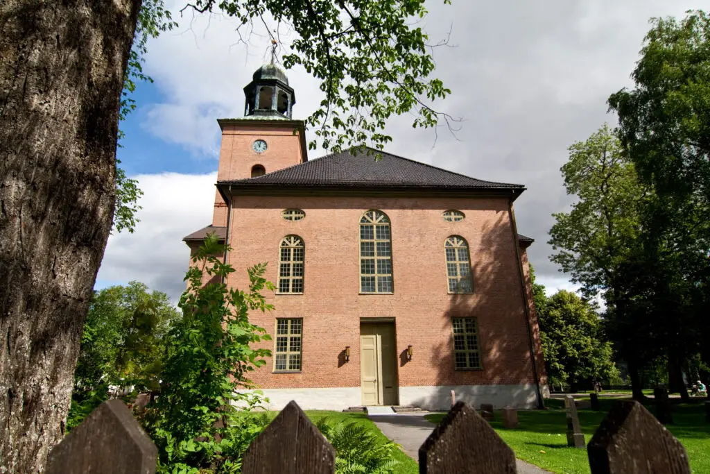 Historic Kongsberg Church surrounded by lush greenery in Norway, a prime example of local heritage and architecture.