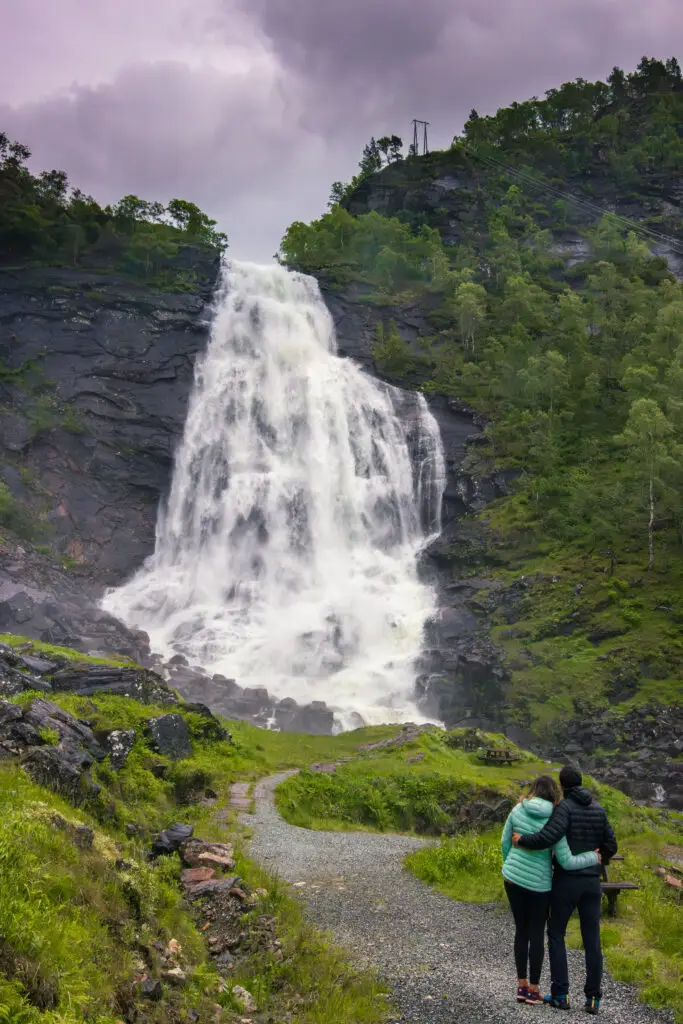 Couple enjoying the view of Fossen Bratte waterfall in Bergen, Norway, highlighting the majestic waterfall and lush greenery.