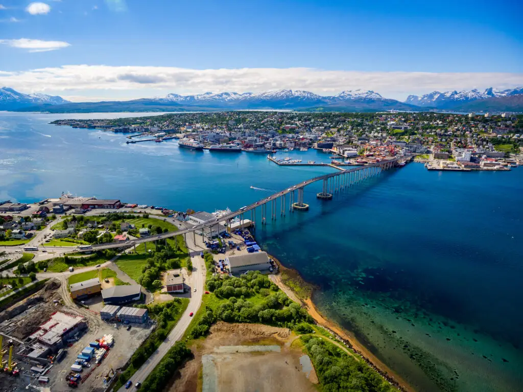 Aerial view of Tromso Bridge connecting the island of Tromsøya with the mainland, surrounded by the stunning landscape of mountains and clear waters in Tromso, Norway.