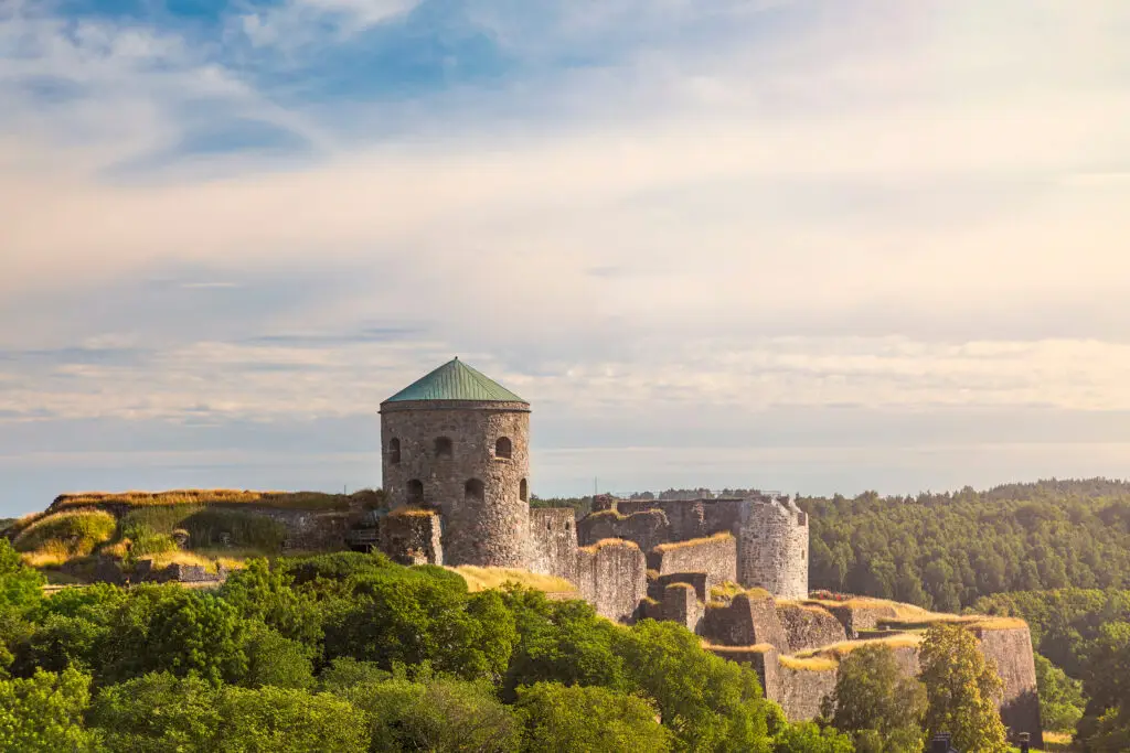 Scenic view of Bohus Fortress ruins on a hillside, surrounded by lush greenery under a soft sky, a popular historical attraction in Scandinavia for tourists.