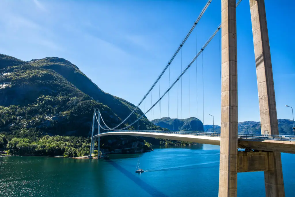 Stunning view of a modern suspension bridge over a serene fjord in Norway, surrounded by lush mountains and clear blue skies on a sunny summer day, perfect for travel and exploration.