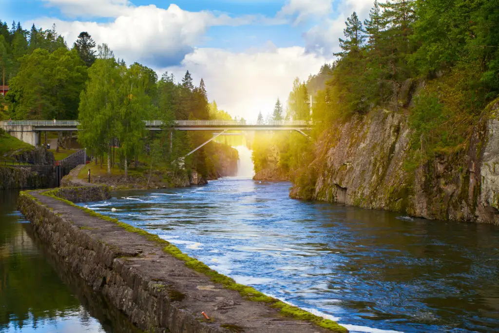 Scenic view of the historic Telemark Canal with old locks, surrounded by forested cliffs under a bright sunlit sky in Skien, Norway - a popular tourist destination