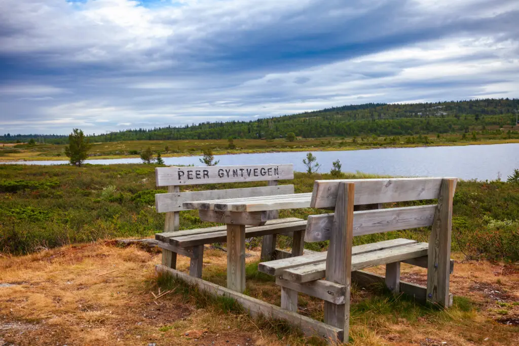 Wooden picnic table with Peer Gynt Vegen carved into it, overlooking a scenic lake and lush landscape in Oppland, Norway
