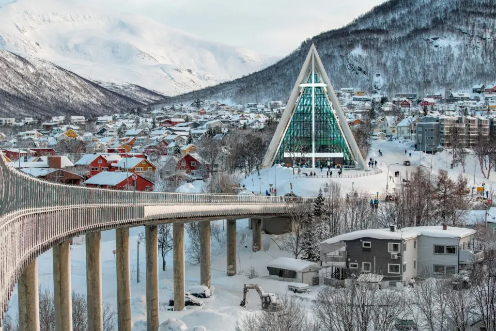 Winter view of the Arctic Cathedral and Tromso Bridge covered with snow, overlooking the colorful houses in Tromso, Norway.