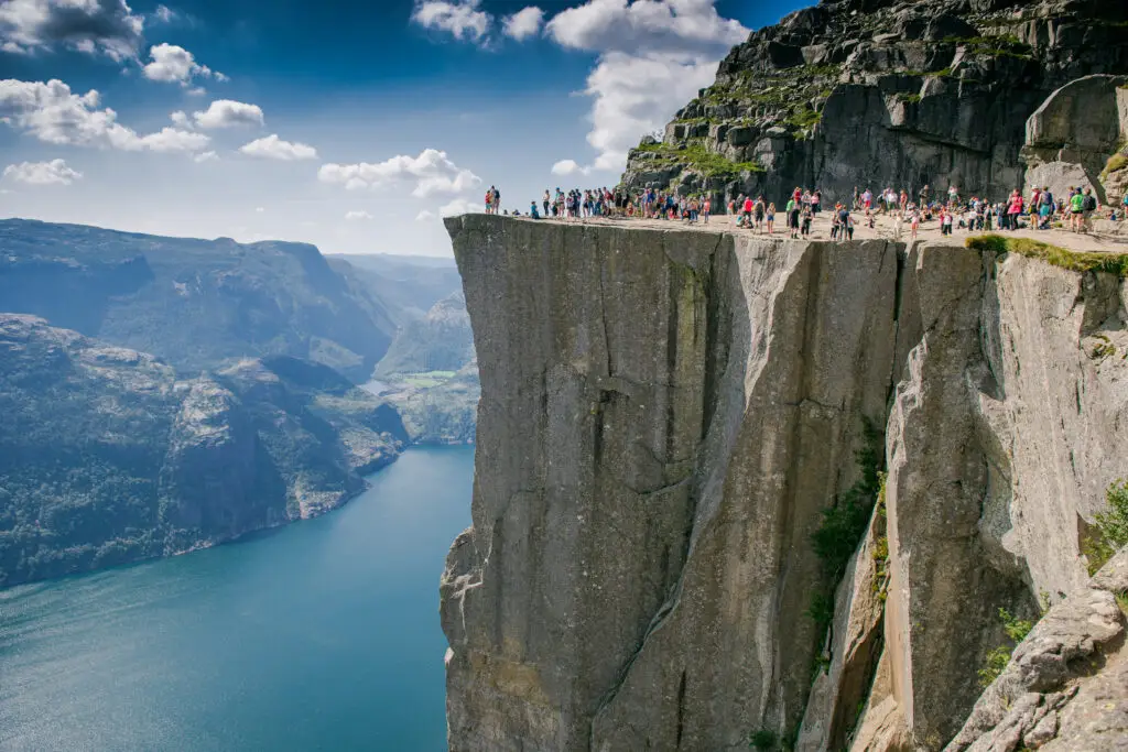 Tourists enjoying the breathtaking view from Preikestolen (Pulpit Rock) overlooking the fjord in the mountains of Norway.