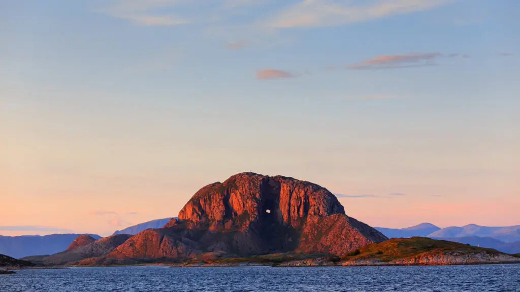 Sunset illuminating Torghatten Mountain in Norway, showcasing its distinctive natural tunnel and surrounding seascape.