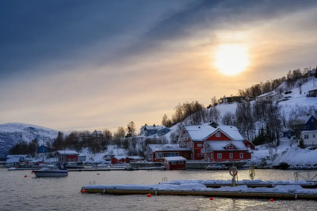 Scenic view of Lyngseidet village harbor at sunset, featuring colorful waterfront houses against a backdrop of snowy mountains in Northern Norway.