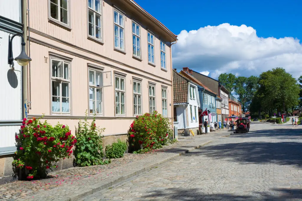 Charming cobblestone street in the Old Town of Fredrikstad, Norway, featuring traditional colorful wooden houses and blooming red roses.