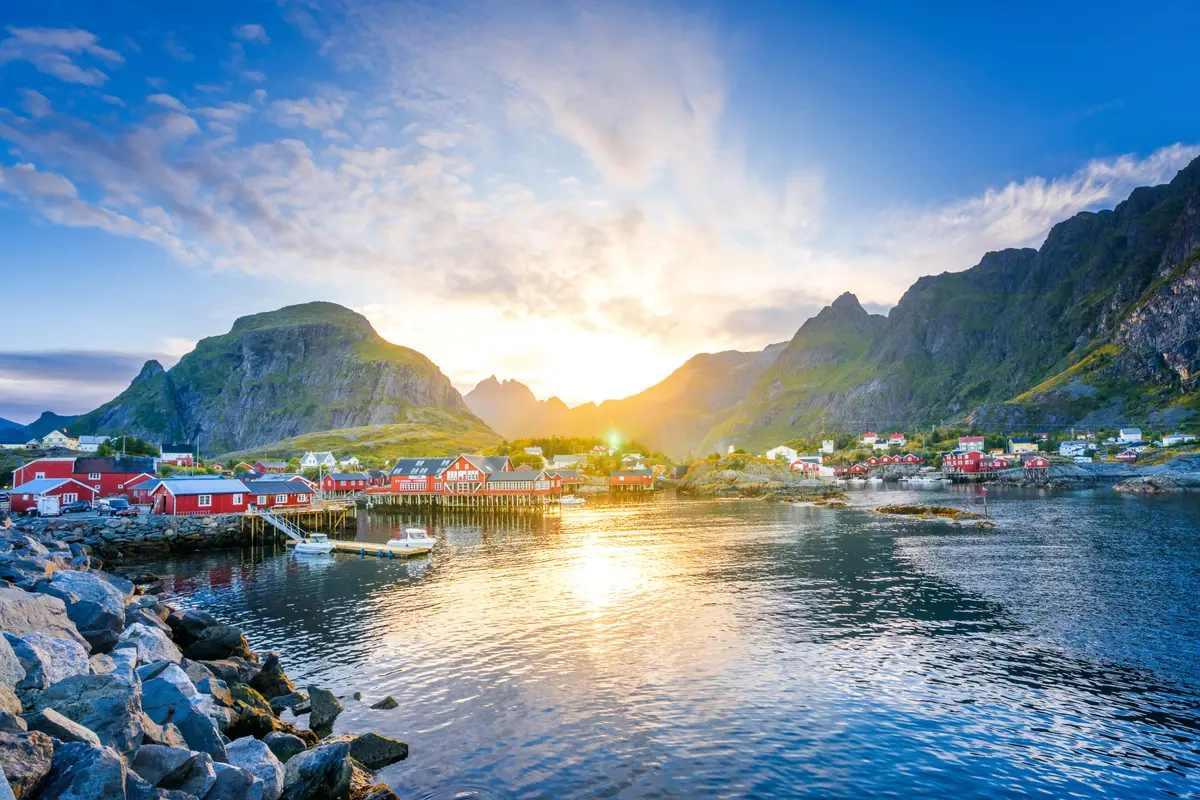 Sunset over the picturesque fishing village of Moskenesøy in Lofoten, Norway, showcasing traditional red wooden houses and rugged mountains.