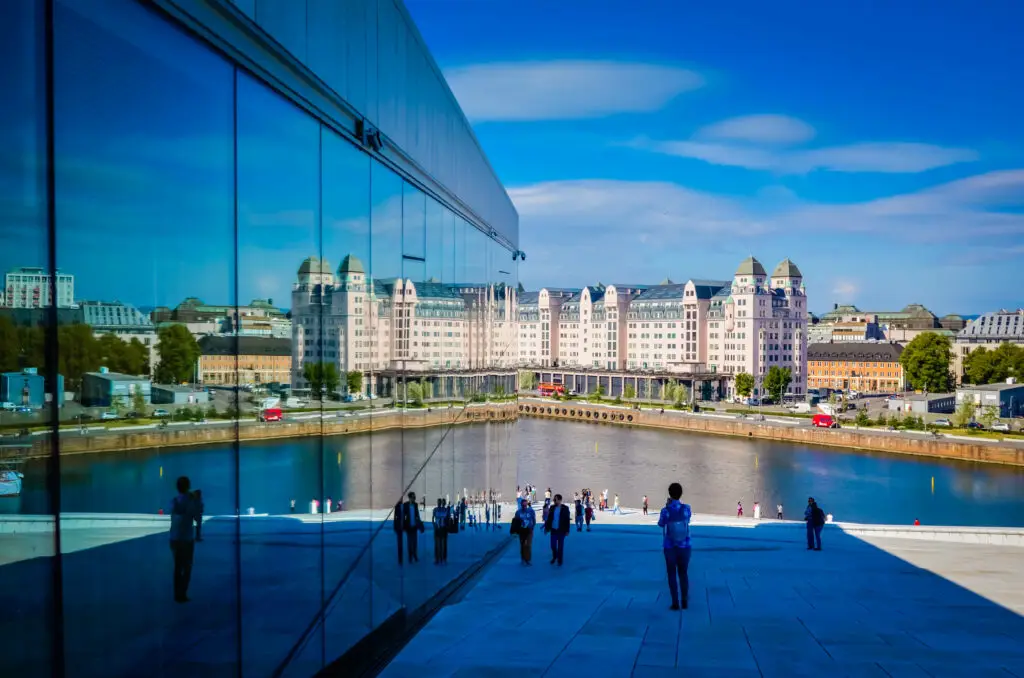 Tourists exploring the Oslo Opera House with reflections of the cityscape and waterfront in Norway.